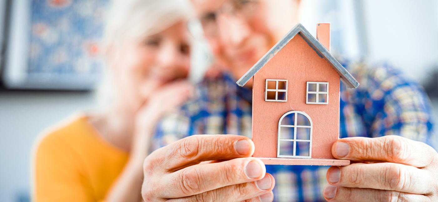 older couple holding a small model of a house