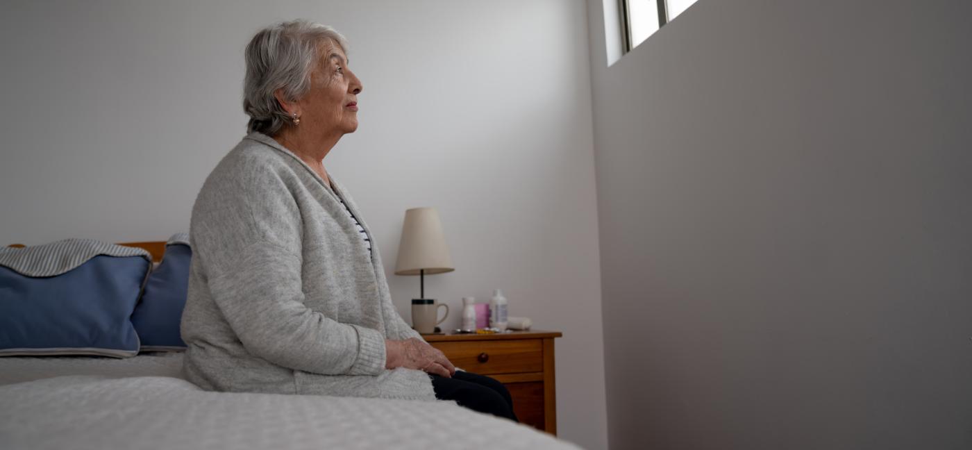 Older adult woman sitting on bed looking at window