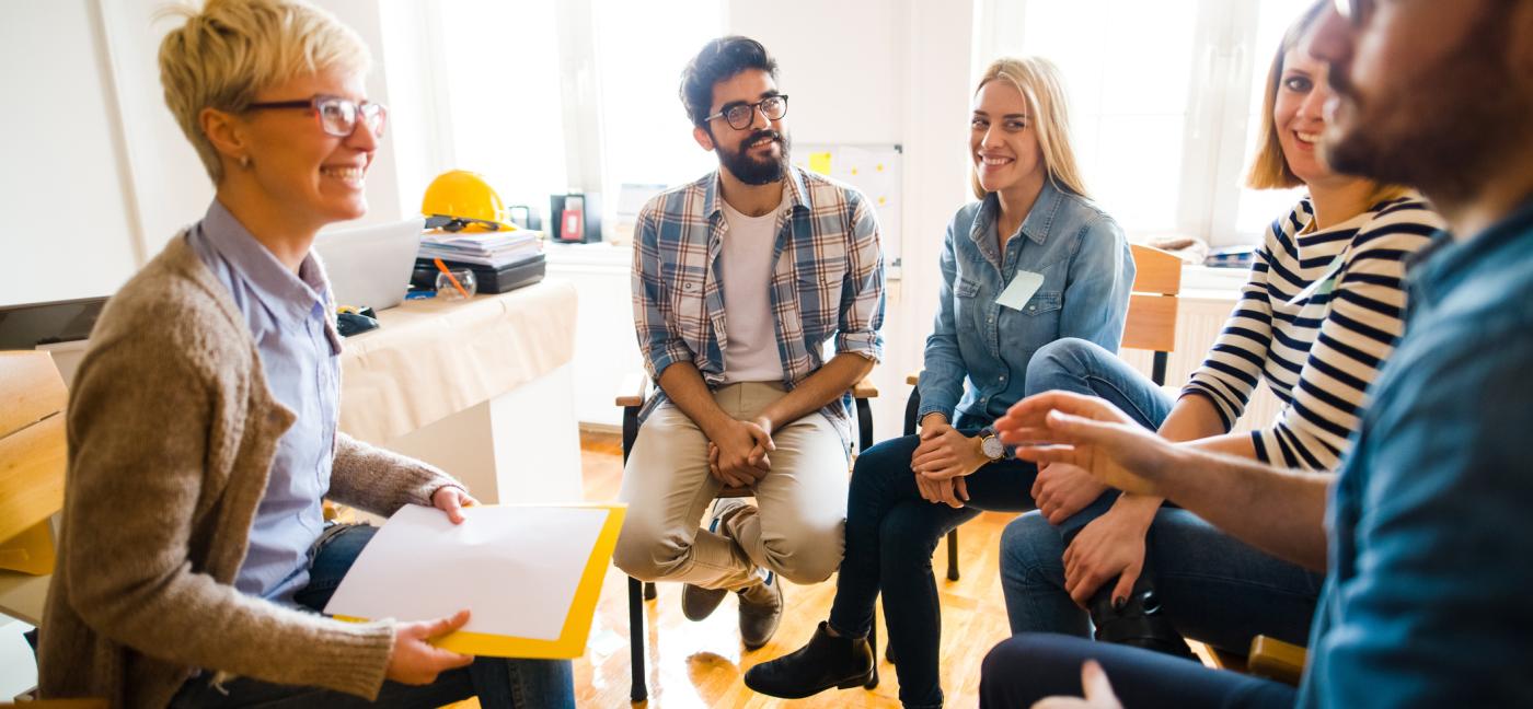 Group of people sitting in a circle on group therapy. Looking at their therapist and listening to her story