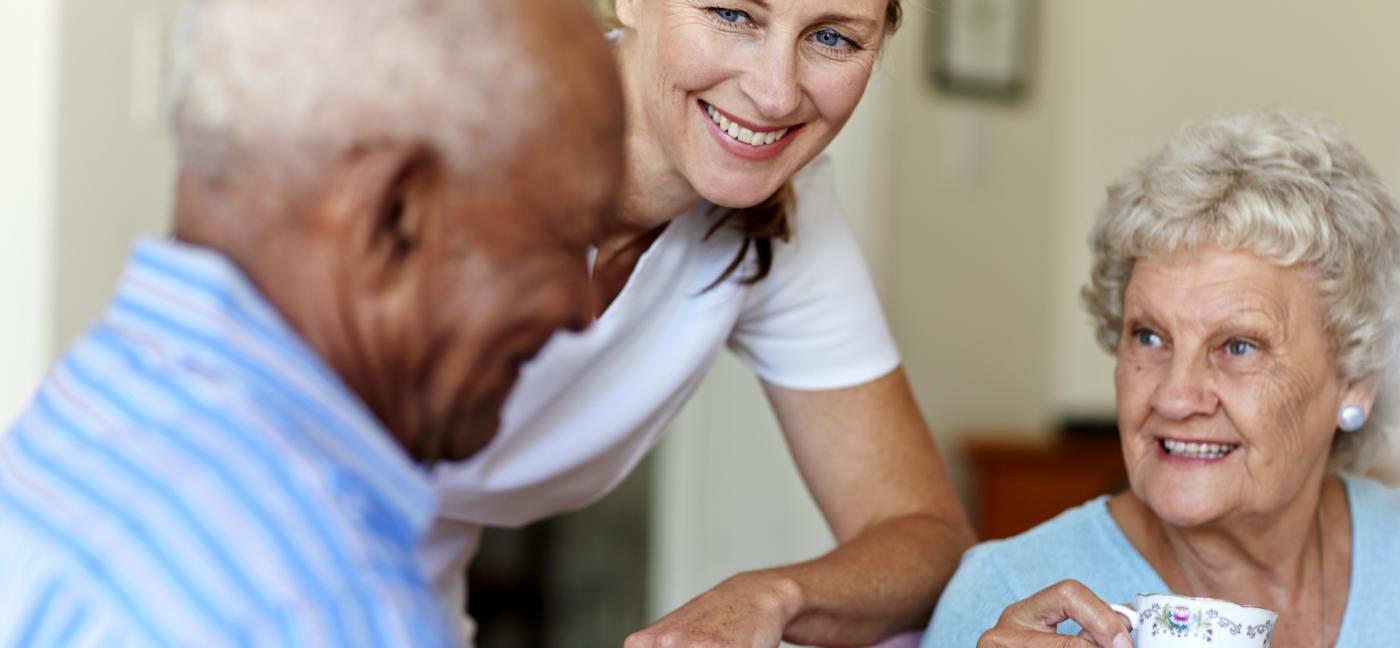 Happy female caretaker with senior people having coffee