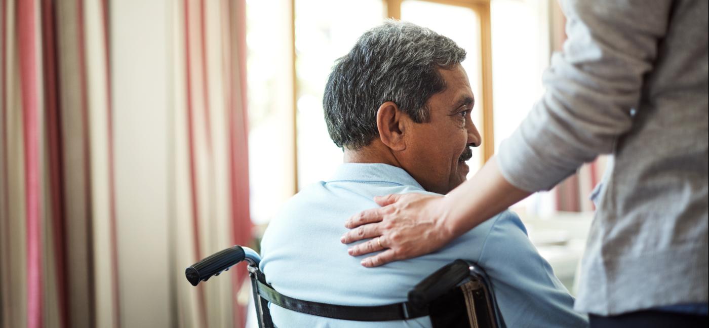 A hand rests on the shoulder of a person in a wheelchair