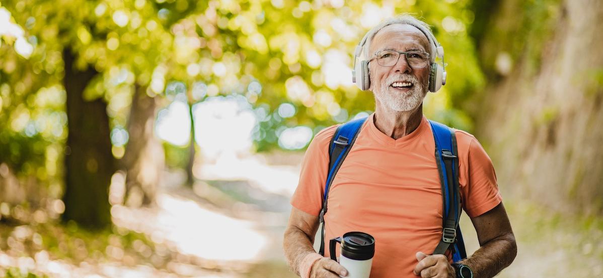 older man with headphones walking happily in the park