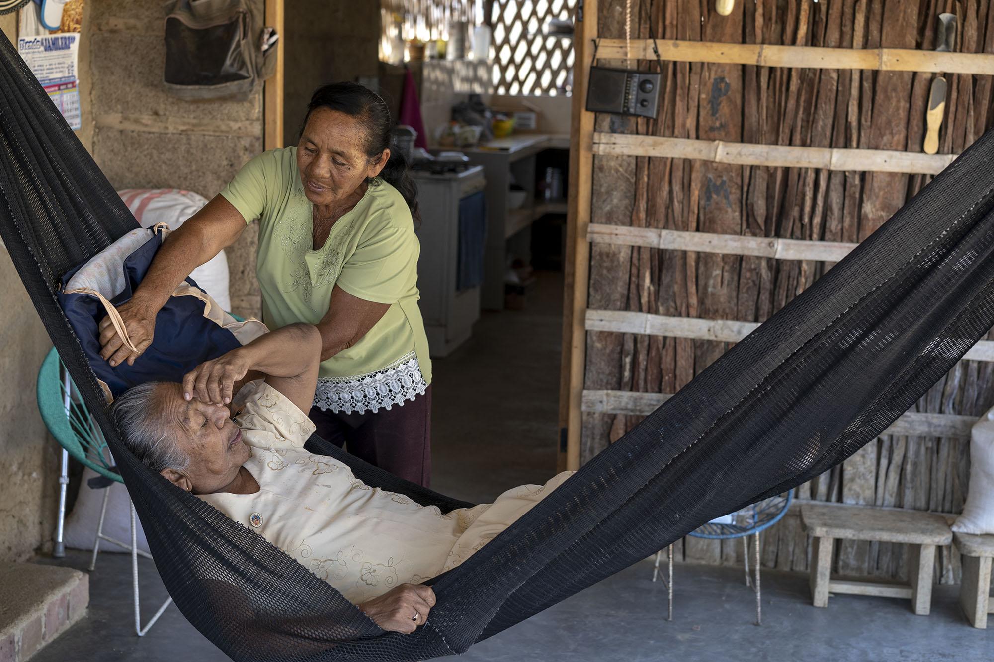 A woman cares for an older adult woman in a hammock in peru