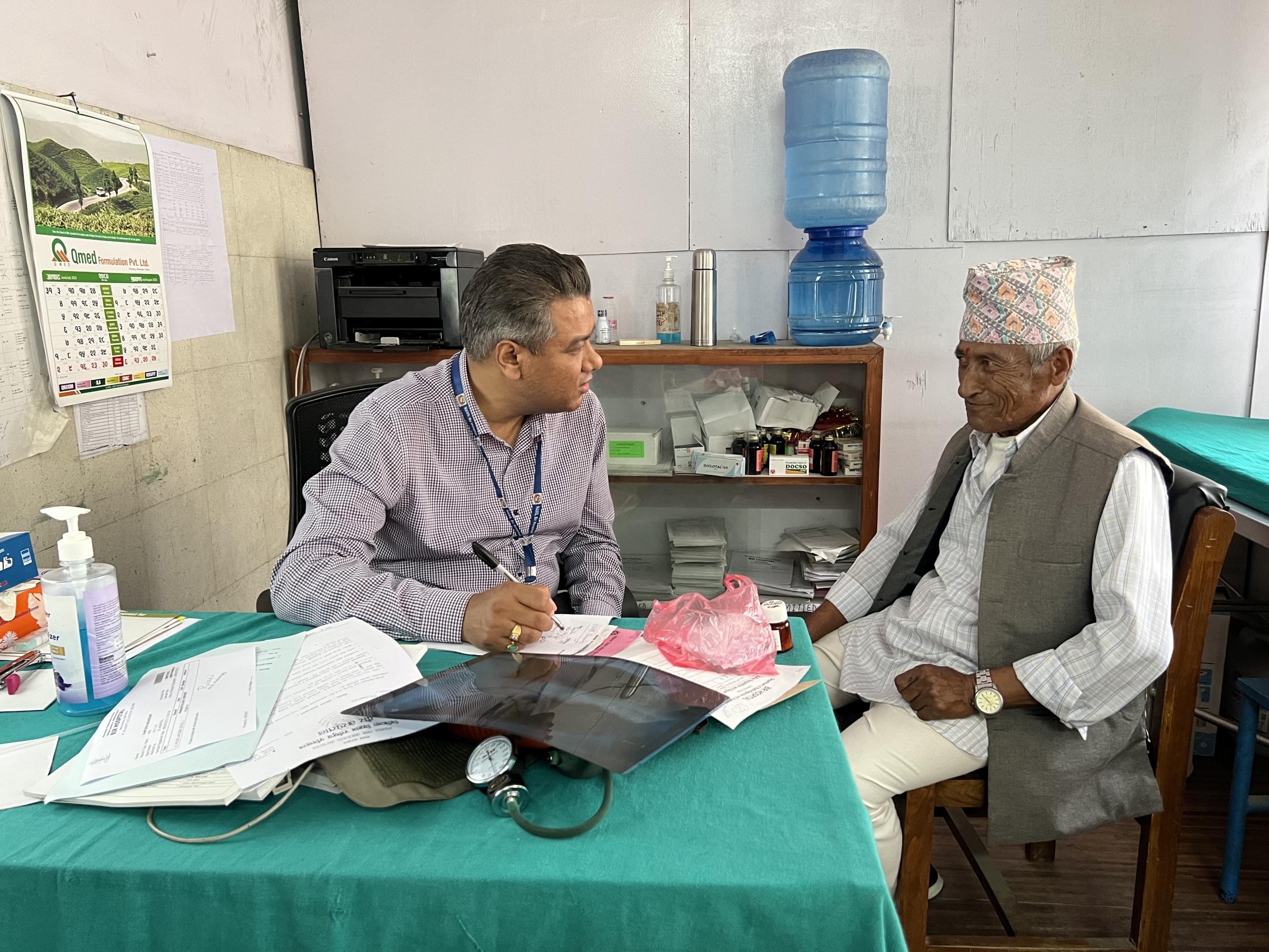 Umesh Bogatil talks with an elderly man wearing traditional dress during a health check-up.