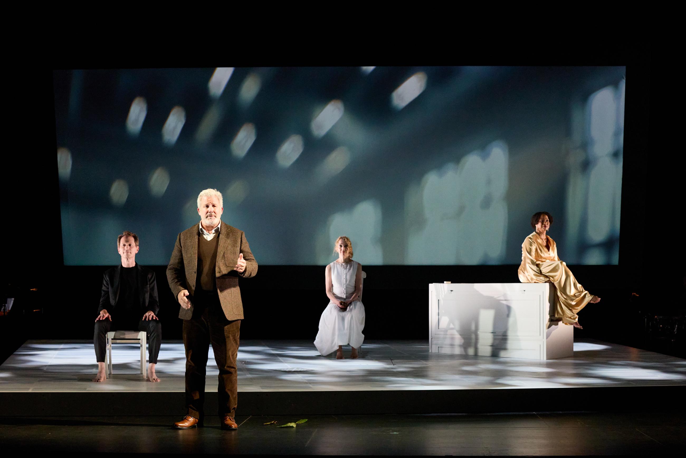 Four actors perform on stage during the UnRavelled play at the event, with soft lights and designs projected behind them.