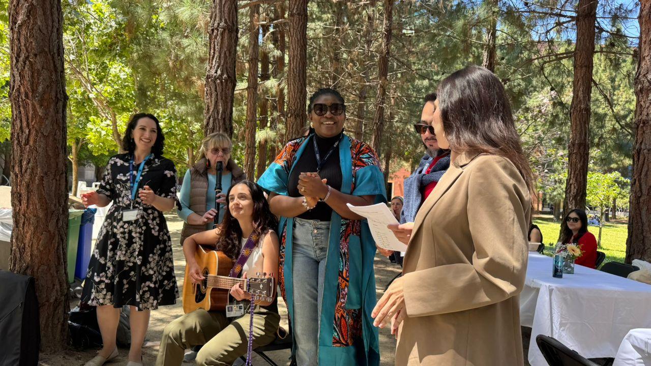 Participants gather outdoors along Feeney Way at UCSF during the GBHI 10-year anniversary celebration, with music, conversation, and community activities beneath a grove of trees.