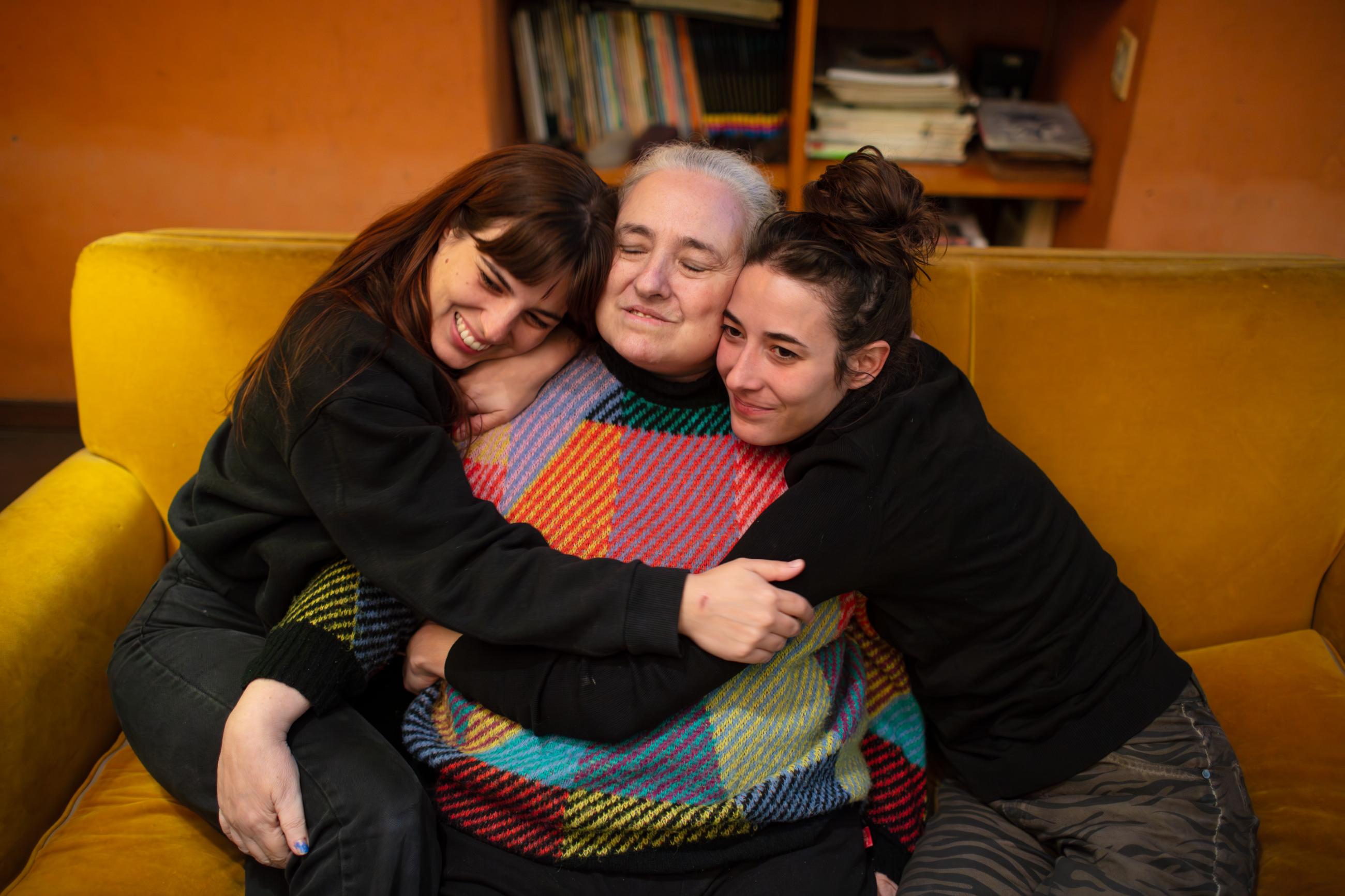 Eugenia Streb sits on a sofa as her daughters, Rosa and Carmen, embrace her.