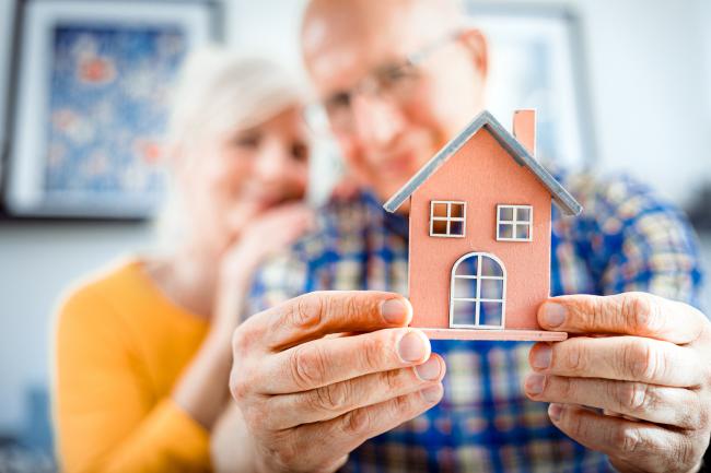 older couple holding a small model of a house