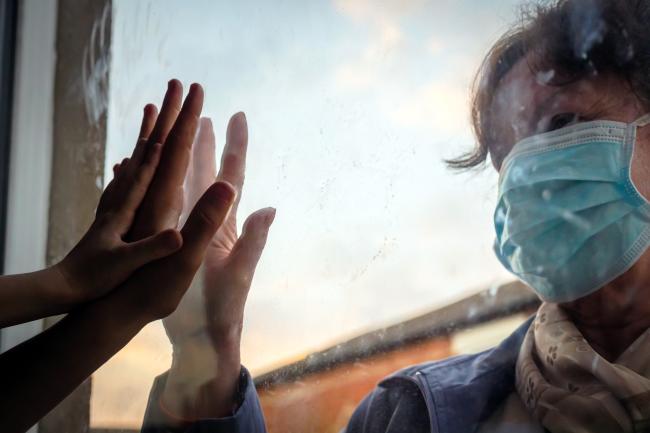 woman with medical mask touching hands through window