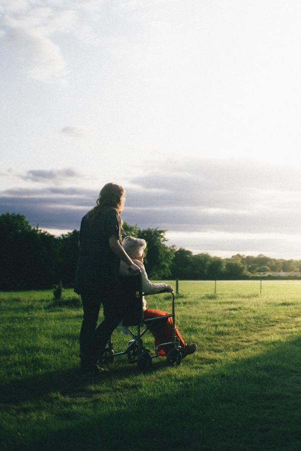Palliative care person pushing older adult in wheelchair outside
