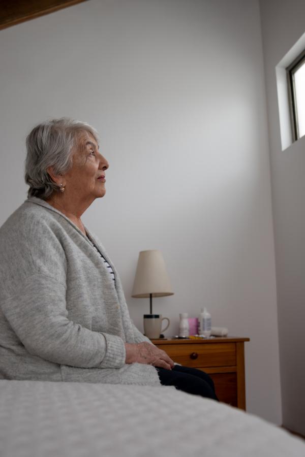 Older adult woman sitting on bed looking at window
