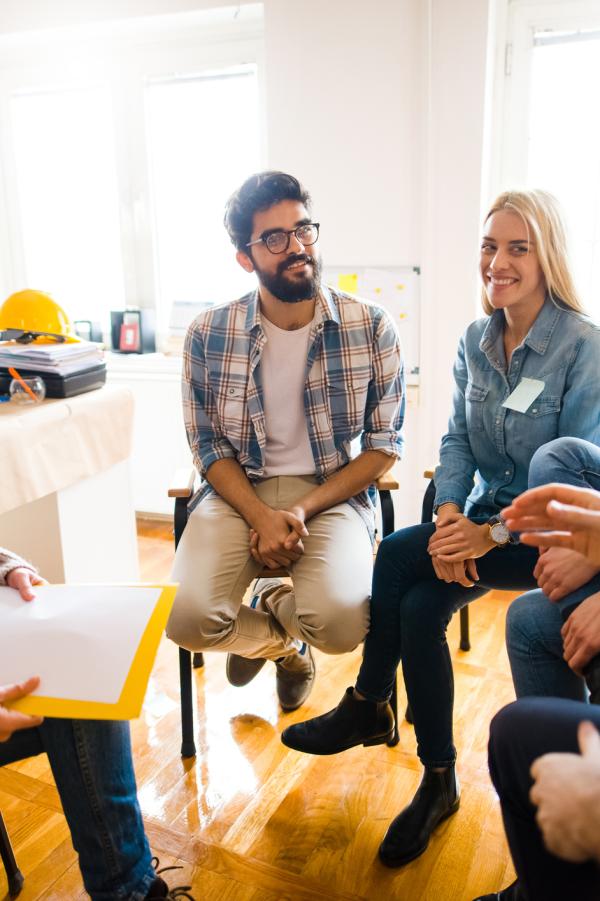 Group of people sitting in a circle on group therapy. Looking at their therapist and listening to her story