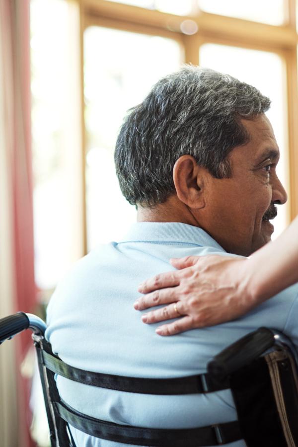A hand rests on the shoulder of a person in a wheelchair