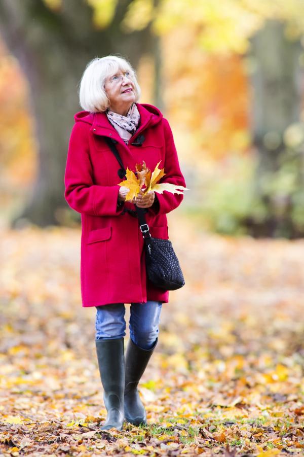 Senior woman is enjoying an independent walk through the autumn woods. She is collecting leaves and enjoying the views.