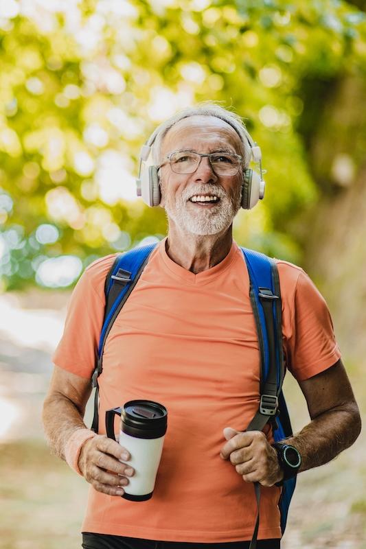 older man with headphones walking happily in the park