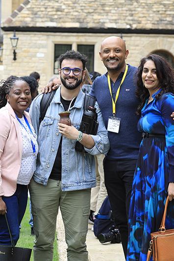 Four fellows stand together smiling in a crowded courtyard at the Oxford convening.