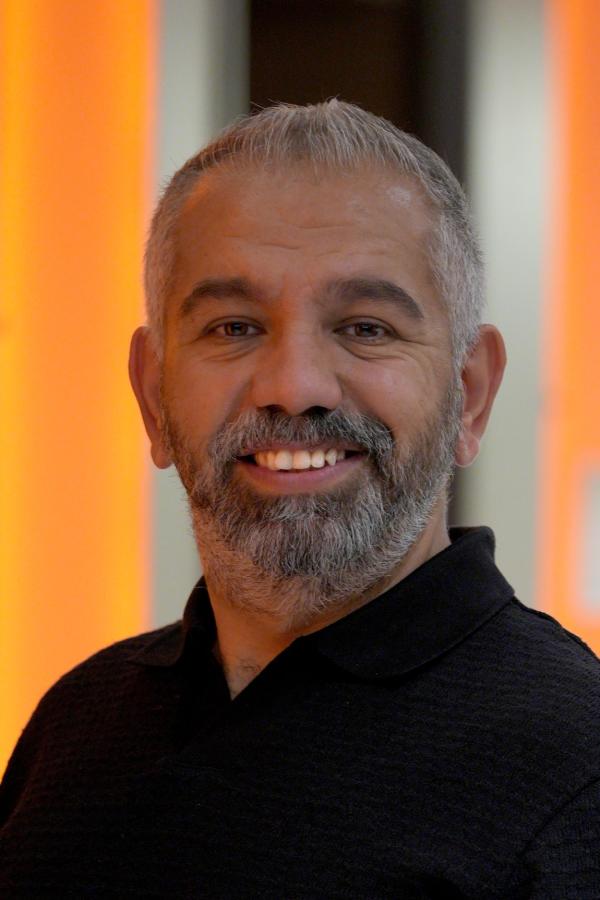 Armağan Uysal smiles at the camera, wearing a black polo shirt and light trousers.