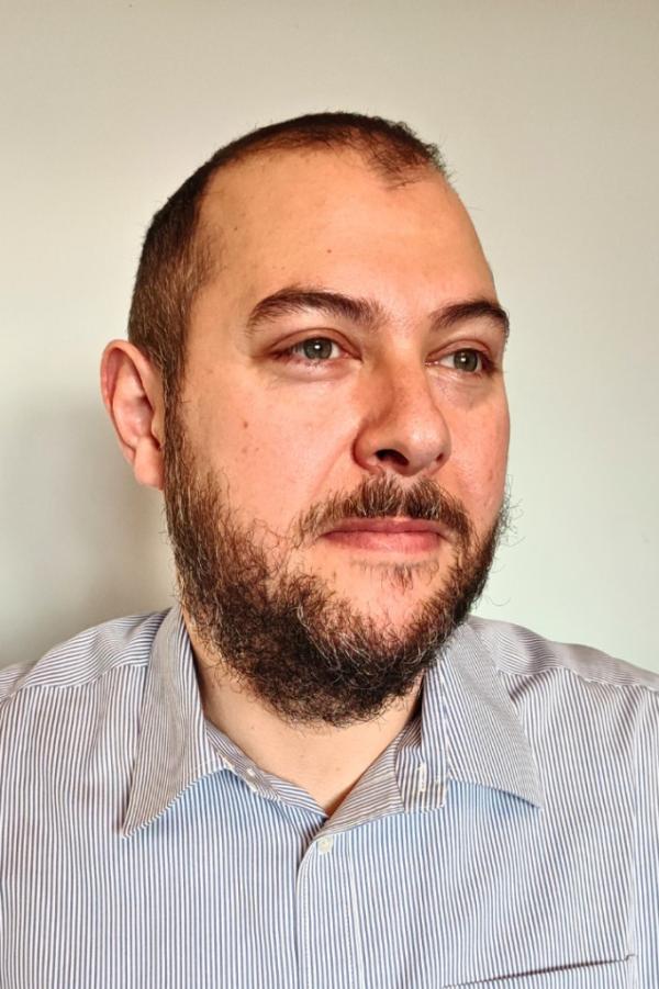 Stelios Zygouris wearing a light striped shirt and looking slightly to the side.