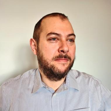 Stelios Zygouris wearing a light striped shirt and looking slightly to the side.