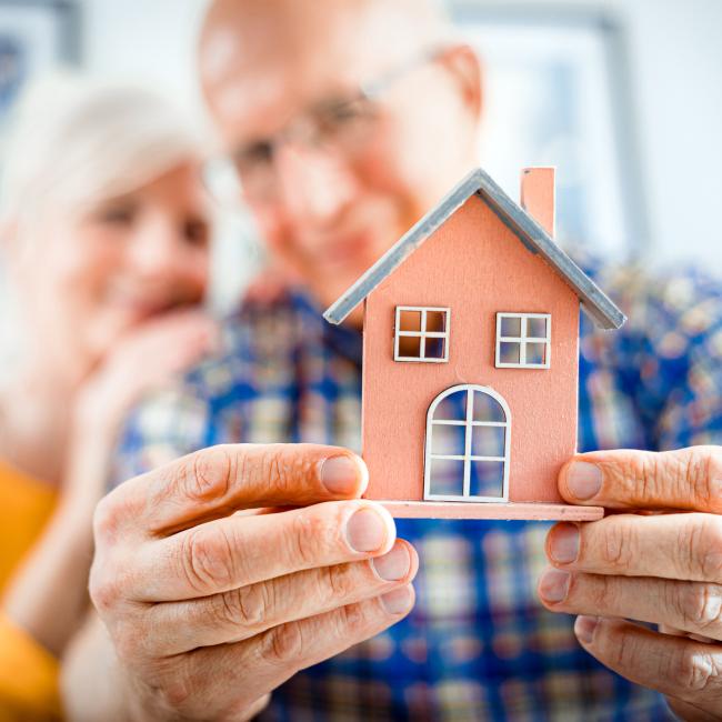 older couple holding a small model of a house