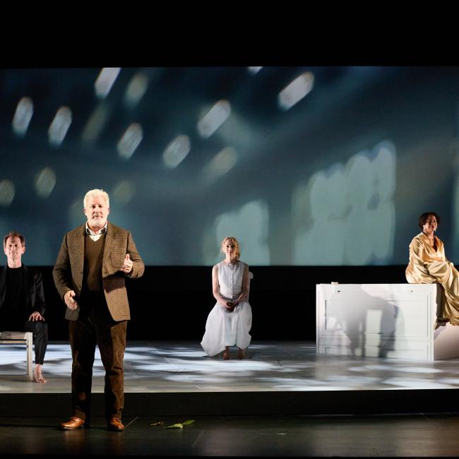 Four actors perform on stage during the UnRavelled play at the event, with soft lights and designs projected behind them.