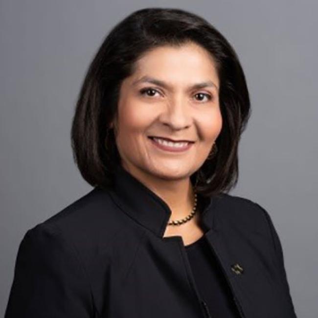 Professional headshot of a woman smiling, wearing a dark blazer against a neutral background.