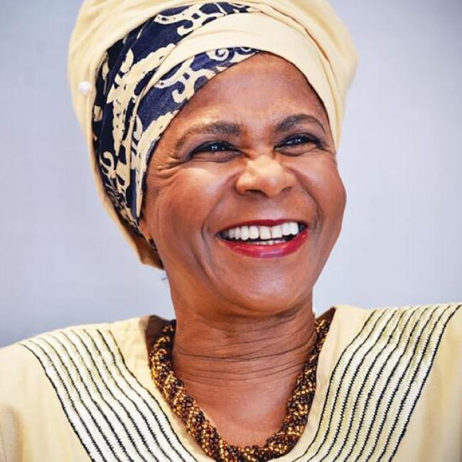 Portrait of Mamphela Ramphele smiling, wearing a patterned headwrap and traditional attire.