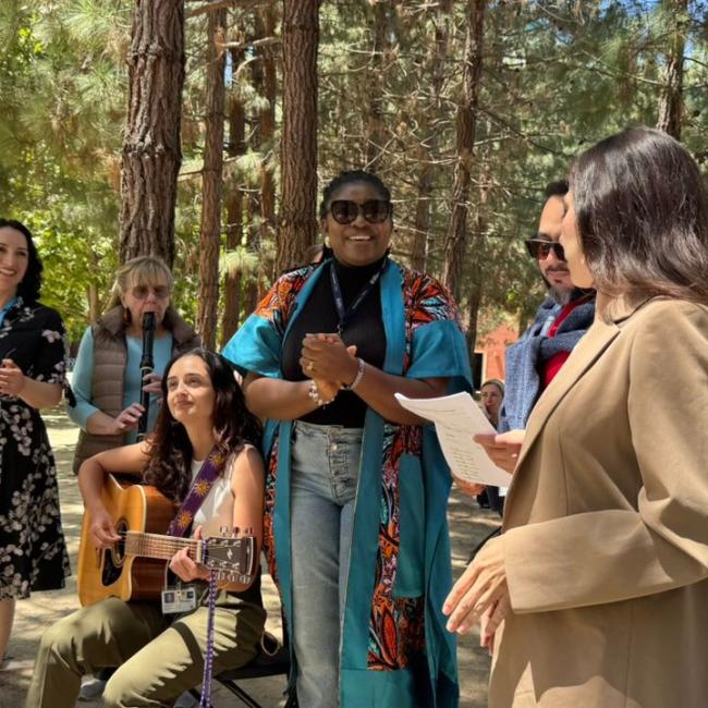 Participants gather outdoors along Feeney Way at UCSF during the GBHI 10-year anniversary celebration, with music, conversation, and community activities beneath a grove of trees.