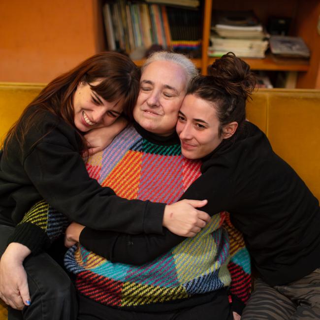 Eugenia Streb sits on a sofa as her daughters, Rosa and Carmen, embrace her.