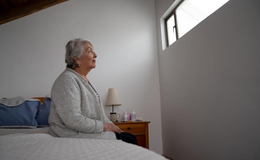 Older adult woman sitting on bed looking at window