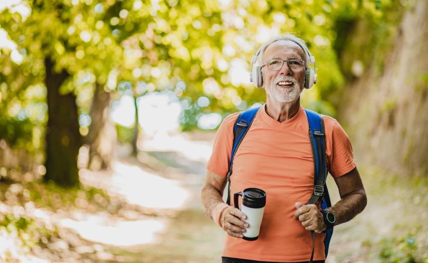 older man with headphones walking happily in the park