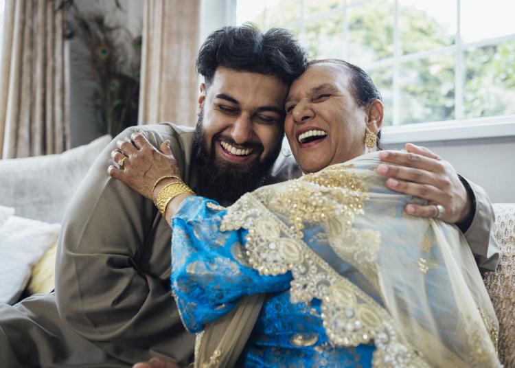 A shot of a grandmother and her grandson embracing while sitting on the sofa, both smiling broadly.