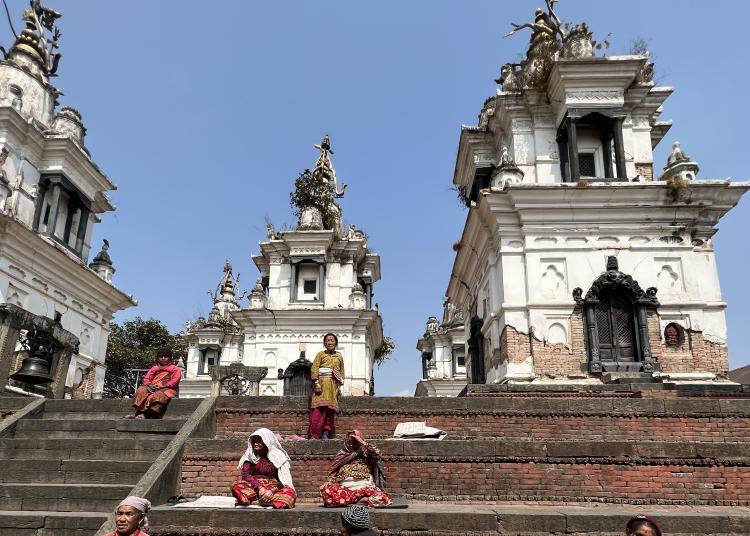 Older women sit and rest on the stone steps of a temple in Nepal.