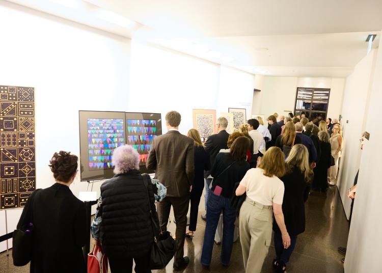 A group of visitors look closely at colorful artwork displayed in the gallery at the UnRavelled event.