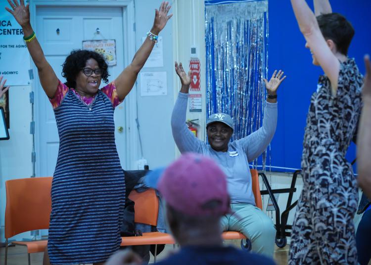 Older adults raise their arms together during a group dance activity in a community center.