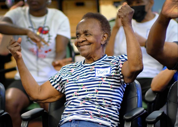 An older woman and a facilitator smile while holding colorful fans during a dance activity.
