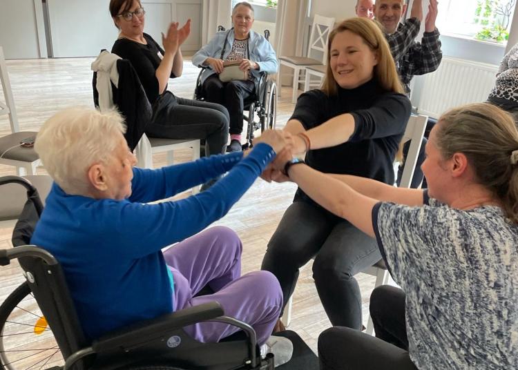 Older adults sit in a circle and hold hands during a group movement activity.