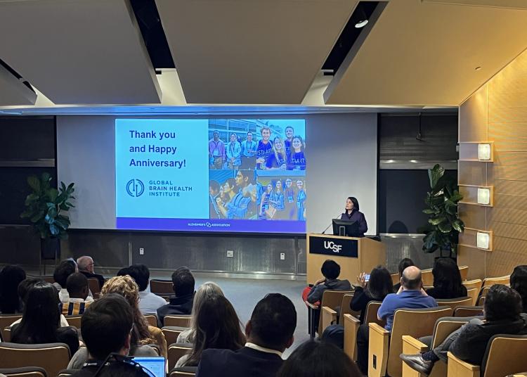 Audience gathers in a UCSF auditorium as a closing slide celebrating GBHI's 10-year anniversary is projected on screen.