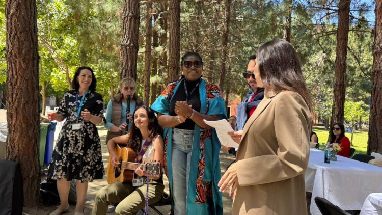 Participants gather outdoors along Feeney Way at UCSF during the GBHI 10-year anniversary celebration, with music, conversation, and community activities beneath a grove of trees.