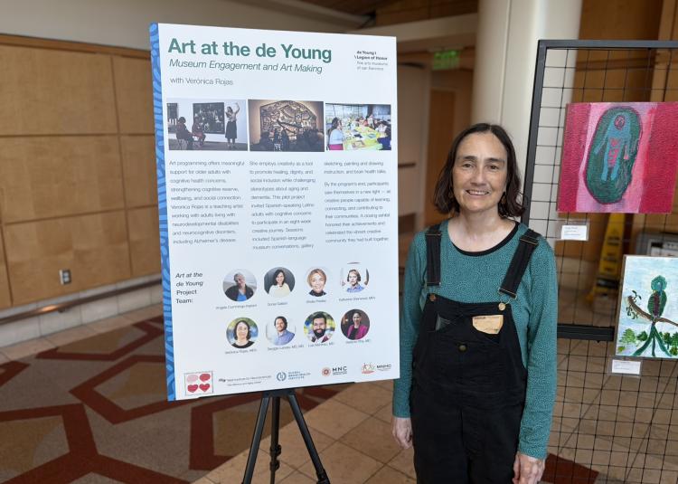 Atlantic Fellow Verónica Rojas stands beside artwork and an exhibit highlighting her de Young Museum arts program with older Latino adults.