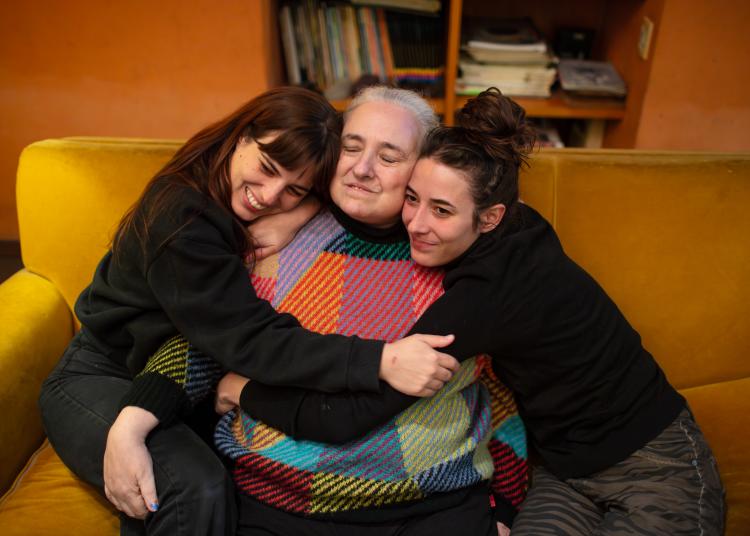 Eugenia Streb sits on a sofa as her daughters, Rosa and Carmen, embrace her.